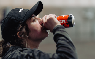 Woman in black hat and black shirt drinking from a red and black vyper energy can