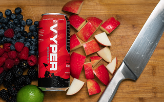 Black and red vyper energy can on cutting board next to knife with blueberries, raspberries, blackberries, an orange, a lime, and chopped apple pieces