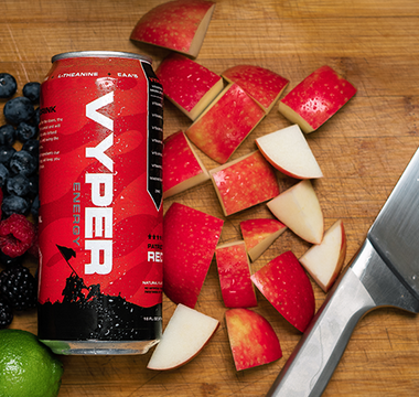 Black and red vyper energy can on cutting board next to knife with blueberries, raspberries, blackberries, an orange, a lime, and chopped apple pieces