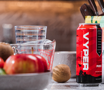 Red and black vyper energy can on kitchen counter with bowl of fruit, measuring cup, and knives