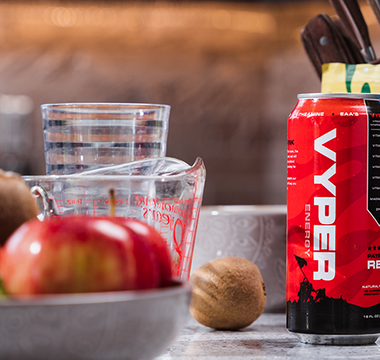 Red and black vyper energy can on kitchen counter with bowl of fruit, measuring cup, and knives