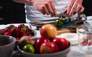Person in kitchen squeezing lime with bowls of apples and strawberries in front of him