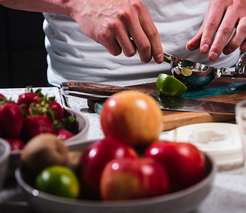 Person in kitchen squeezing lime with bowls of apples and strawberries in front of him