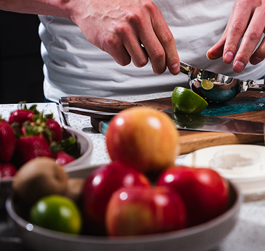 Person in kitchen squeezing lime with bowls of apples and strawberries in front of him