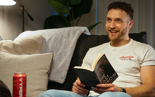 Dayne smiling in his living room sitting on a couch while reading "The Last Arrow" with a Vyper Energy sitting on the table in front of him. 